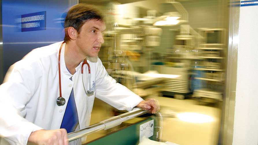 Arzt mit weißem Arbeitskittel beim Schieben eines Patientenbettes beim Notfalleinsatz