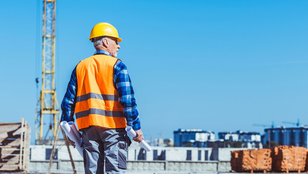 Bauarbeiter mit Signalweste und Helm blickt auf Baustelle