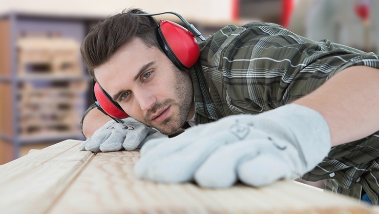 Arbeiter mit Hörschutz inspiziert Holzbrett