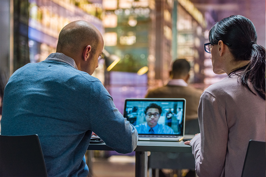 Two people in an office at a video conference via laptop Two people in an office at a video conference via laptop